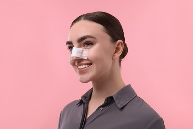 Photo of Woman with medical bandage on her nose after plastic surgery operation against pink background