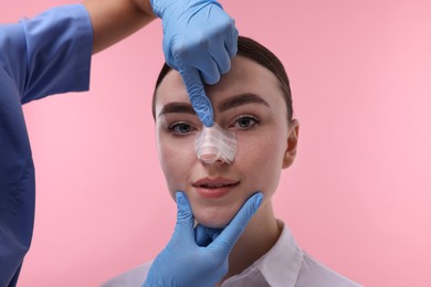 Photo of Doctor checking patient's nose after plastic surgery operation on pink background, closeup