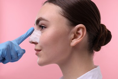 Photo of Doctor checking patient's nose after plastic surgery operation on pink background, closeup