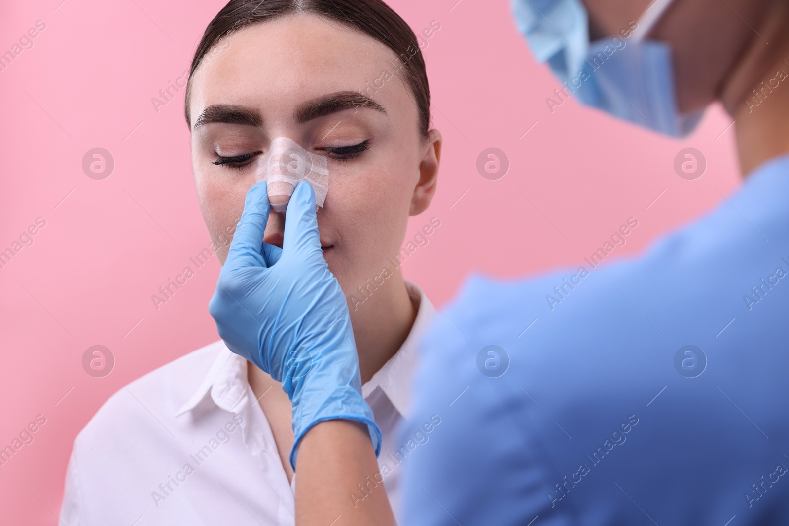 Photo of Doctor checking patient's nose after plastic surgery operation on pink background, closeup