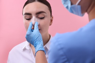 Photo of Doctor checking patient's nose after plastic surgery operation on pink background, closeup