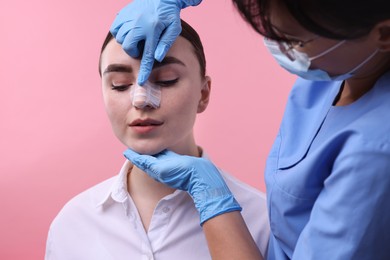 Photo of Doctor checking patient's nose after plastic surgery operation on pink background, closeup