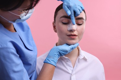 Photo of Doctor checking patient's nose after plastic surgery operation on pink background, closeup