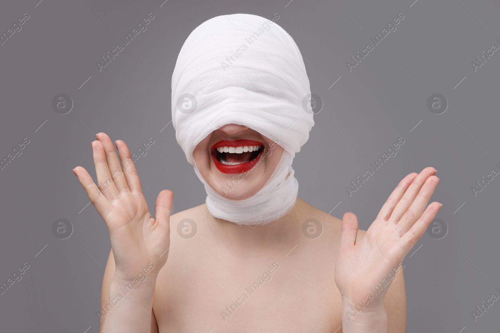 Photo of Woman with face wrapped in medical bandage after plastic surgery operation on grey background