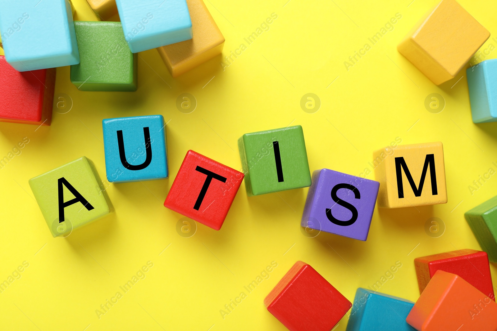 Photo of Word Autism made with colorful cubes on yellow background, flat lay