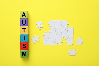 Photo of Word Autism made with colorful cubes and puzzle pieces on yellow background, flat lay