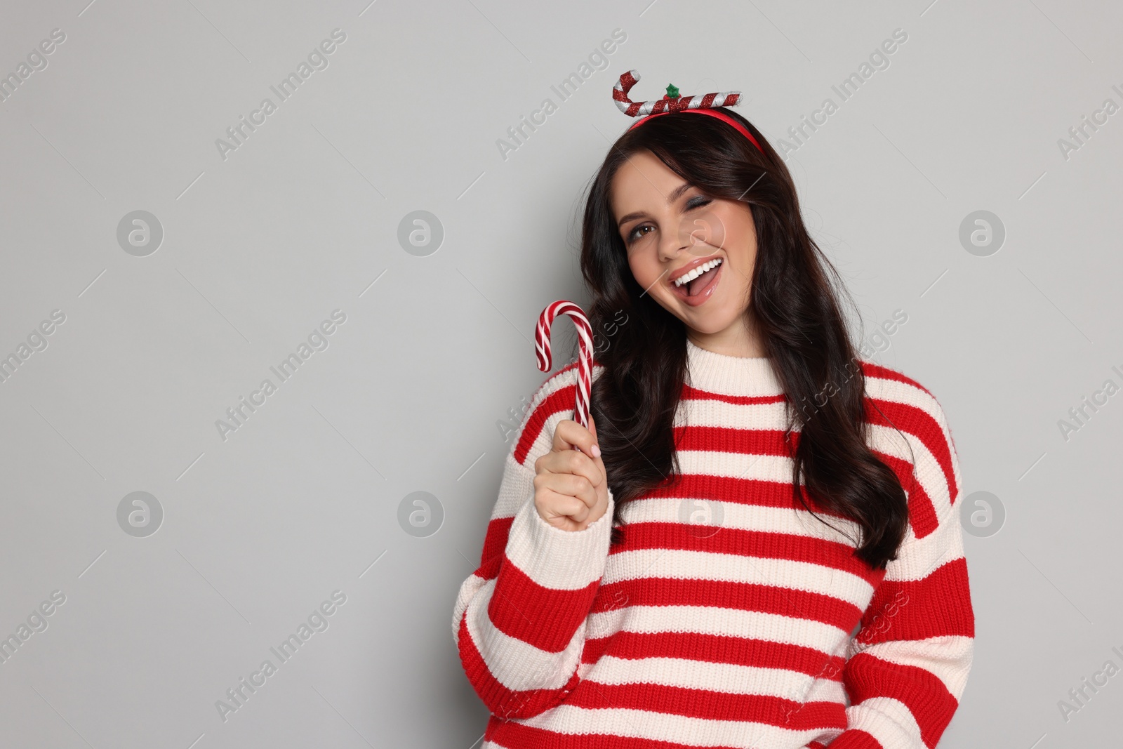 Photo of Happy woman with candy cane on light grey background, space for text. Christmas celebration