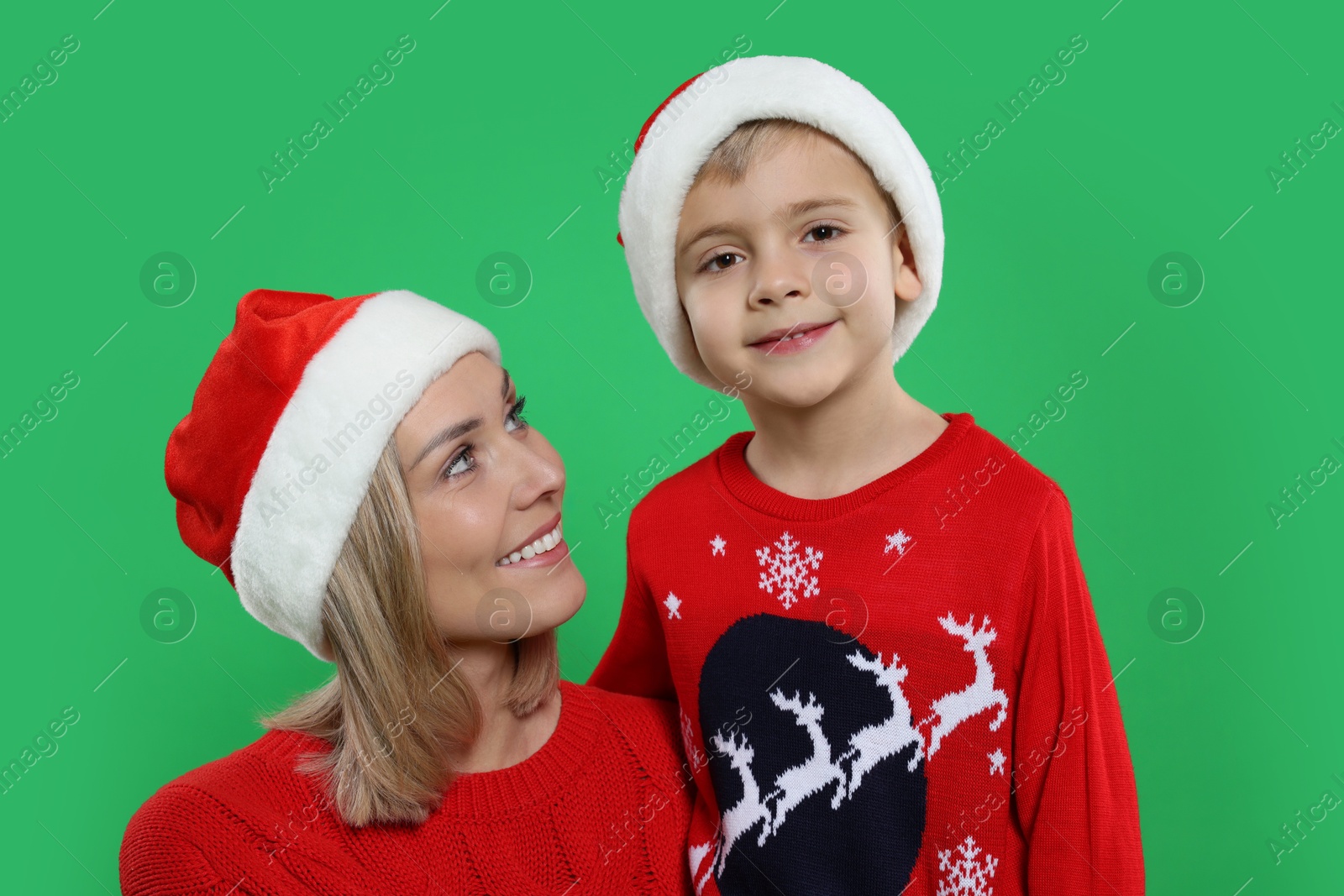 Photo of Mother and son in Santa hats on green background. Christmas celebration