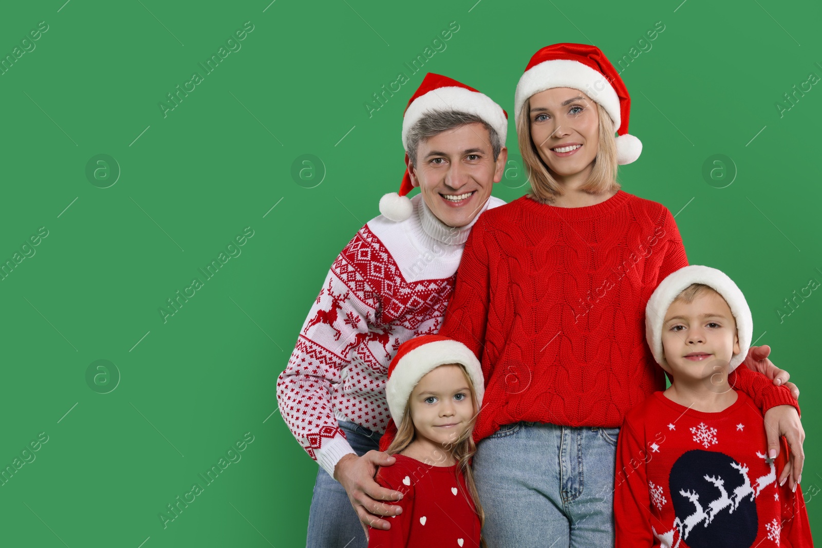 Photo of Happy family in Christmas sweaters and Santa hats on green background. Space for text