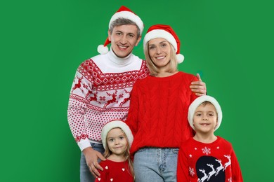 Happy family in Christmas sweaters and Santa hats on green background