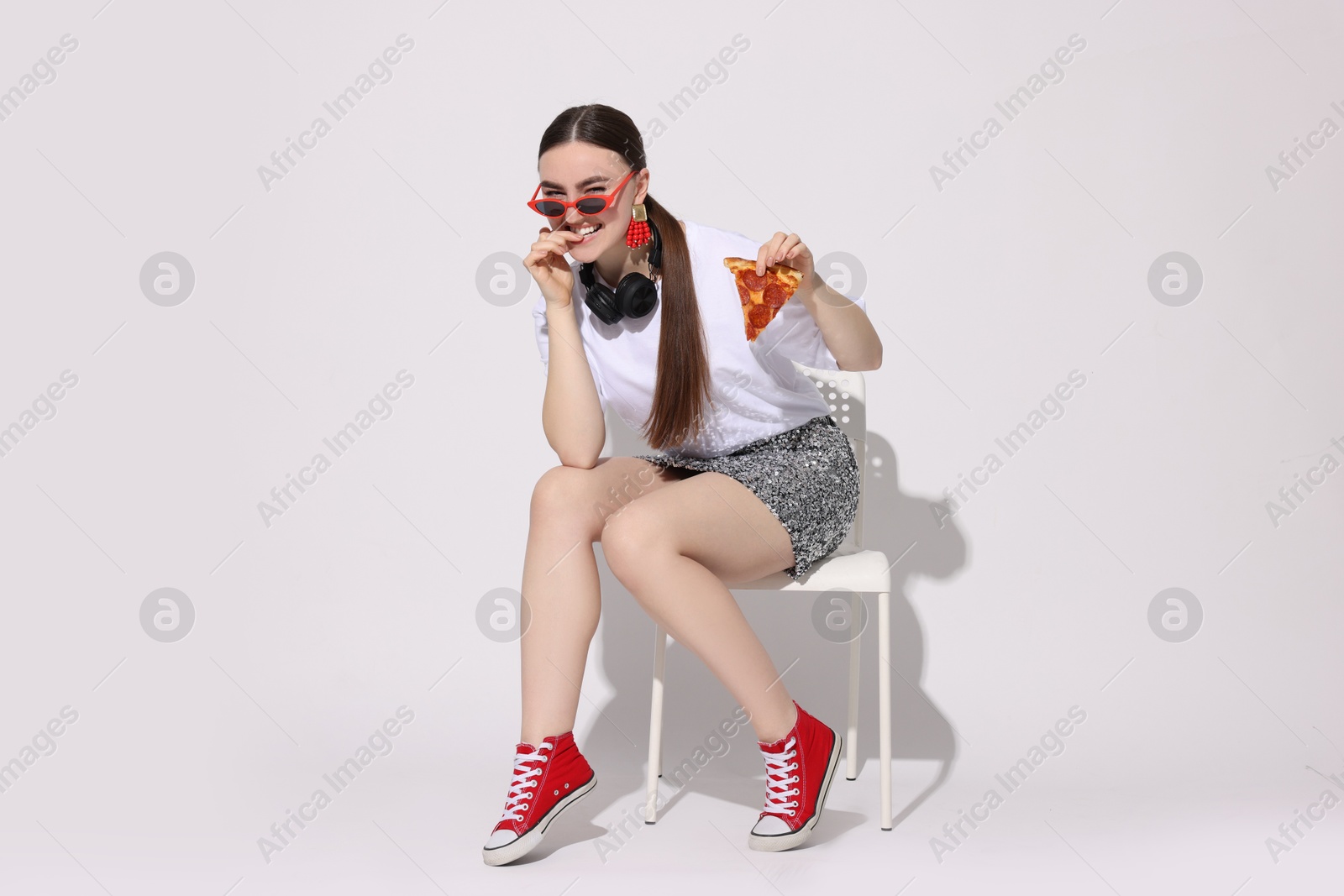 Photo of Woman in sunglasses with piece of pizza sitting on chair against white background