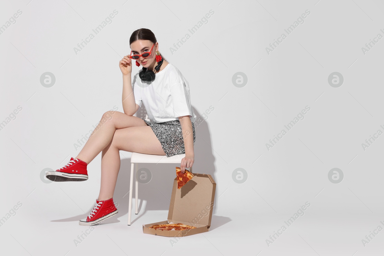 Photo of Woman in sunglasses with delicious pizza sitting on chair against white background, space for text