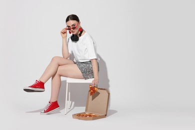 Photo of Woman in sunglasses with delicious pizza sitting on chair against white background, space for text