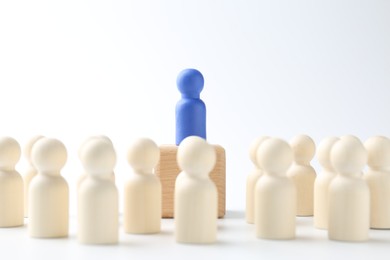 Human figures around wooden block with blue figure on top against white background. Competition concept