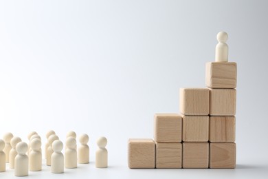 Photo of Human figures in front of stacked wooden blocks with one figure on top against white background. Competition concept