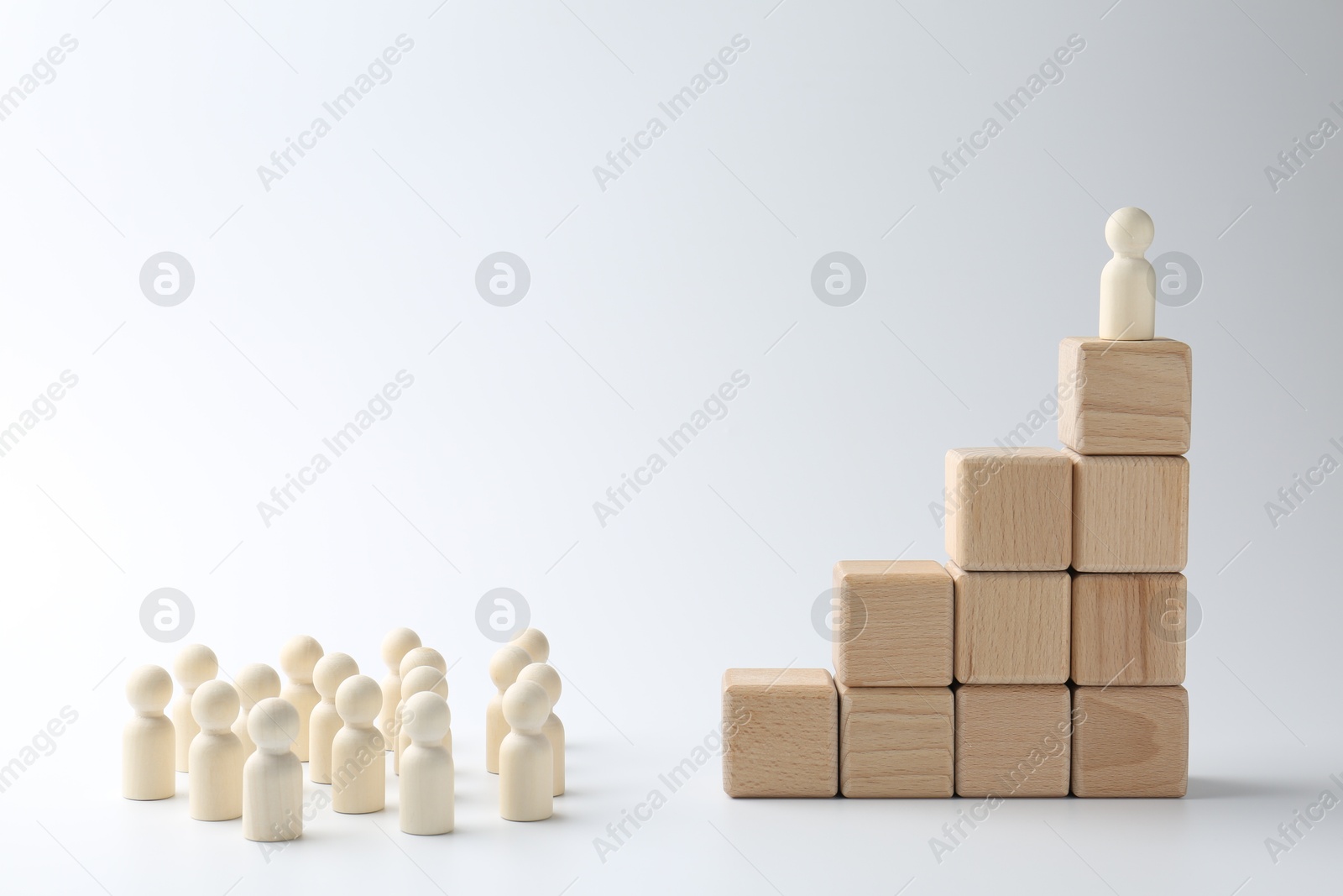 Photo of Human figures in front of stacked wooden blocks with one figure on top against white background. Competition concept