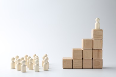 Human figures in front of stacked wooden blocks with one figure on top against white background. Competition concept