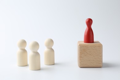 Photo of Human figures in front of wooden block with red figure on top against white background. Competition concept