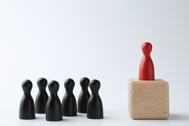 Photo of Human figures in front of wooden block with red figure on top against white background. Competition concept