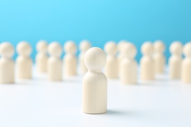 Photo of One human figure standing out among others on white table against light blue background. Competition concept