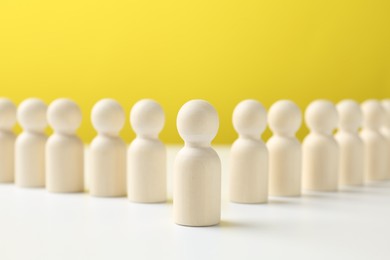 Photo of One human figure standing out among others on white table against yellow background. Competition concept