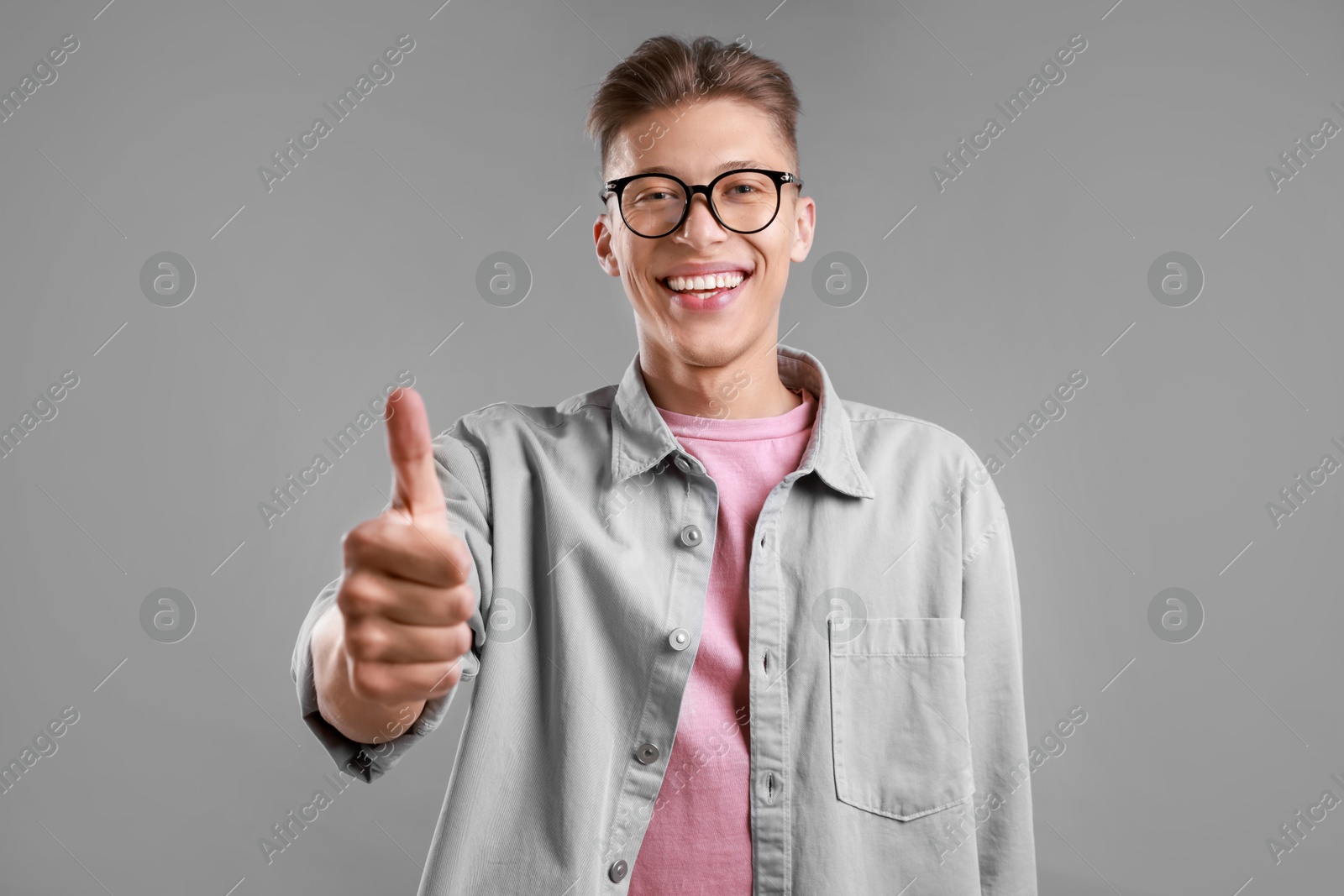 Photo of Happy man showing thumbs up on grey background. Like gesture