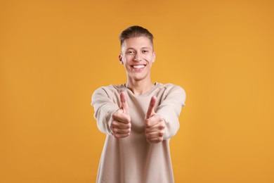 Photo of Happy man showing thumbs up on orange background. Like gesture