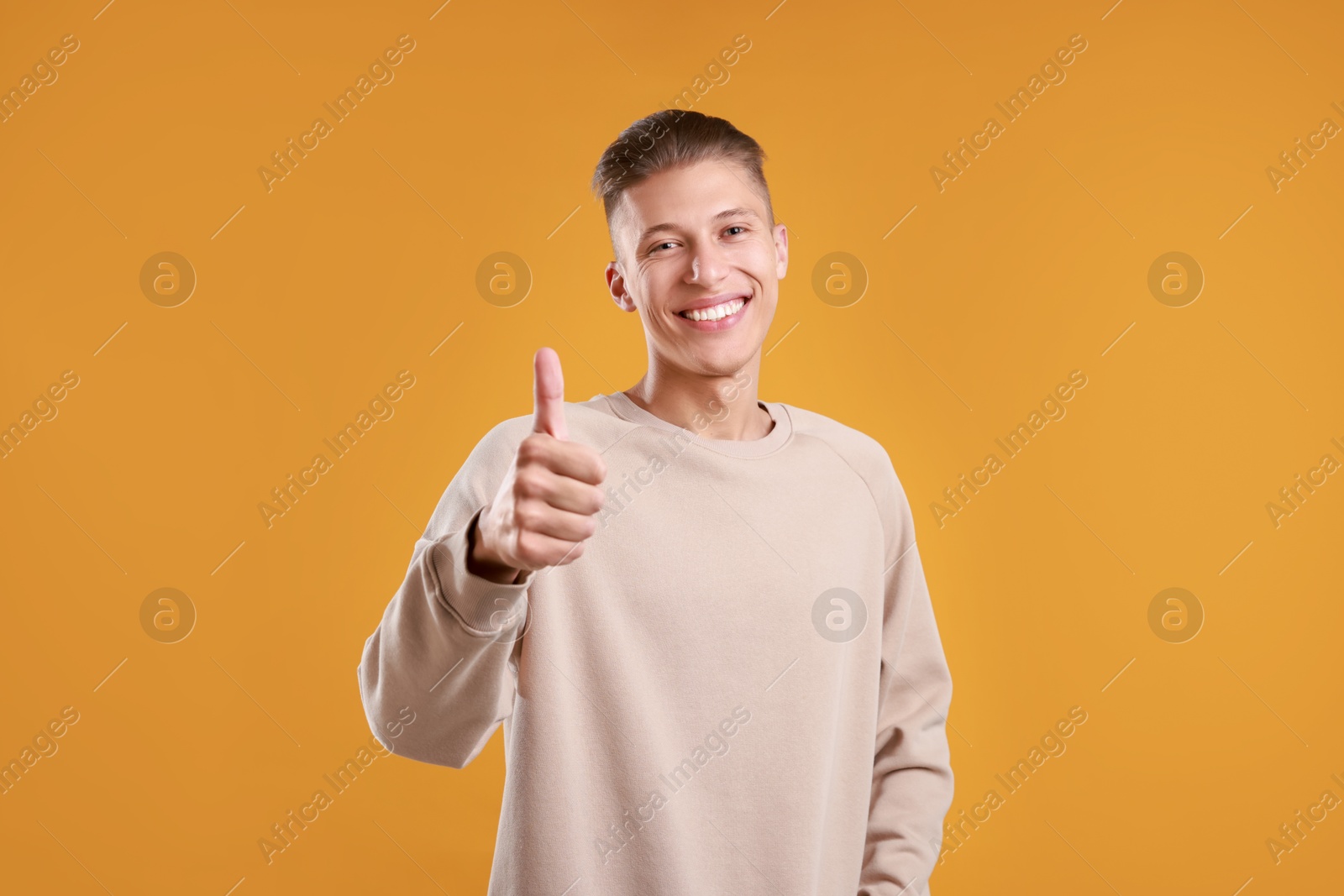 Photo of Happy man showing thumbs up on orange background. Like gesture