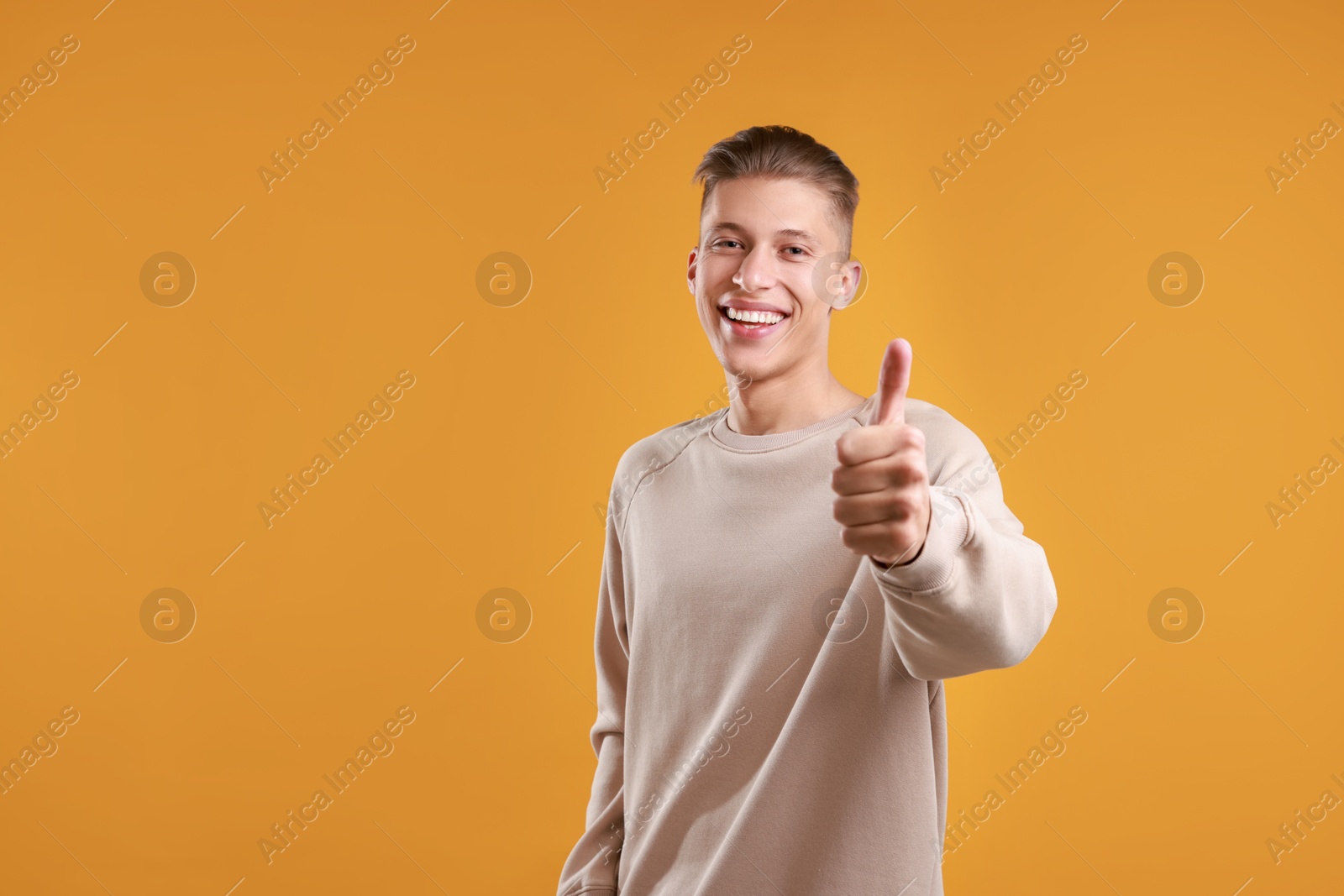 Photo of Happy man showing thumbs up on orange background, space for text. Like gesture