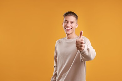 Photo of Happy man showing thumbs up on orange background, space for text. Like gesture