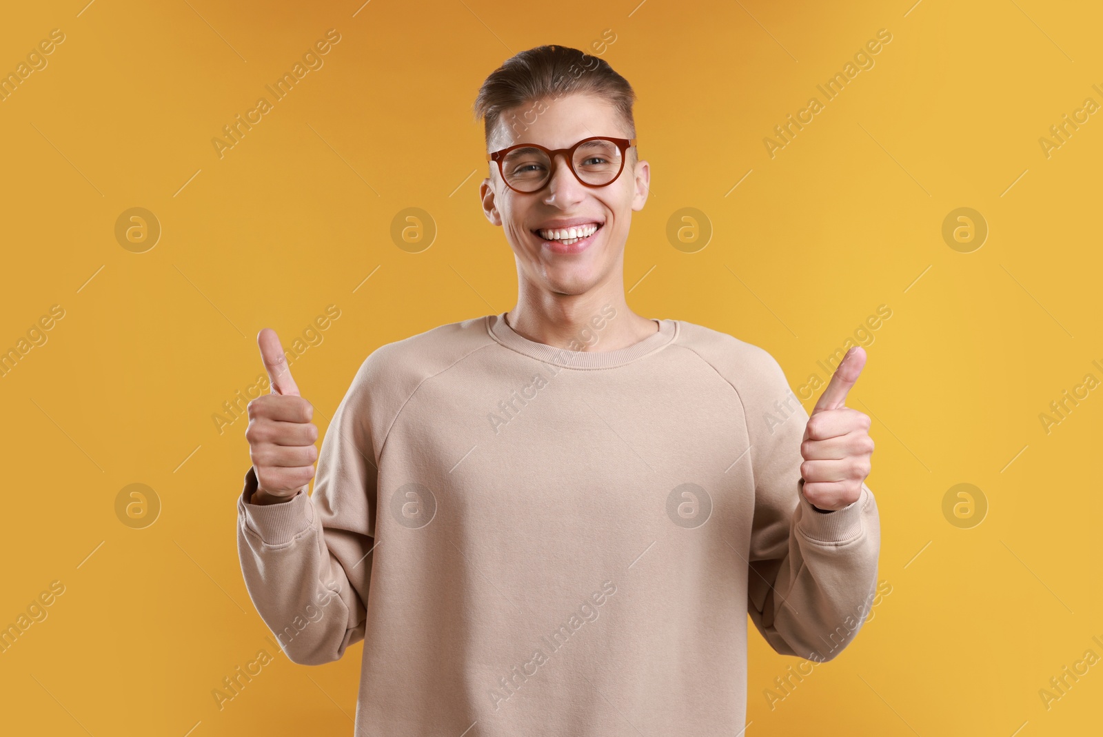 Photo of Happy man showing thumbs up on orange background. Like gesture