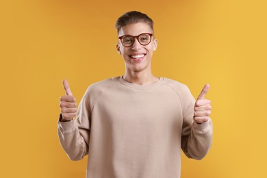 Photo of Happy man showing thumbs up on orange background. Like gesture