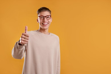 Photo of Happy man showing thumbs up on orange background, space for text. Like gesture