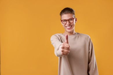 Photo of Happy man showing thumbs up on orange background, space for text. Like gesture