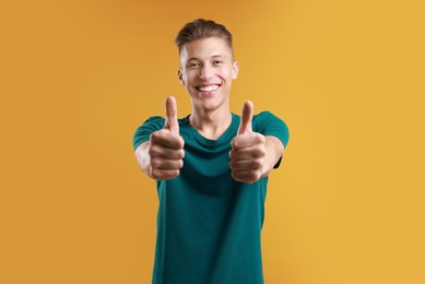 Photo of Happy man showing thumbs up on orange background. Like gesture