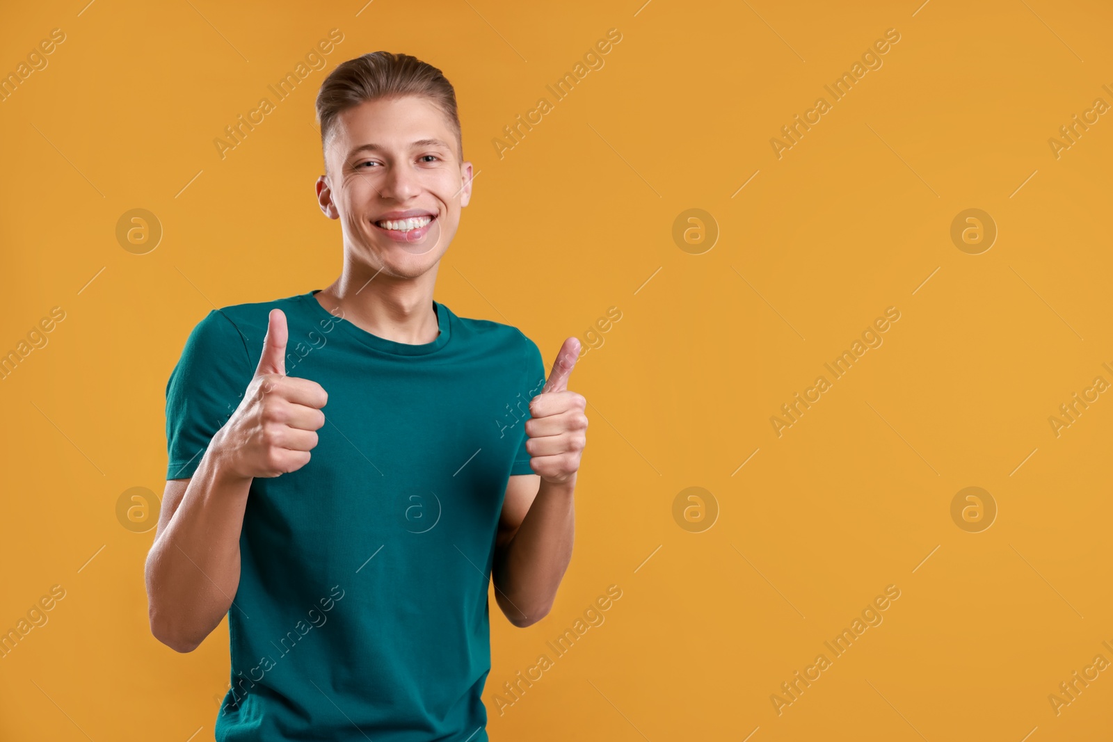 Photo of Happy man showing thumbs up on orange background, space for text. Like gesture