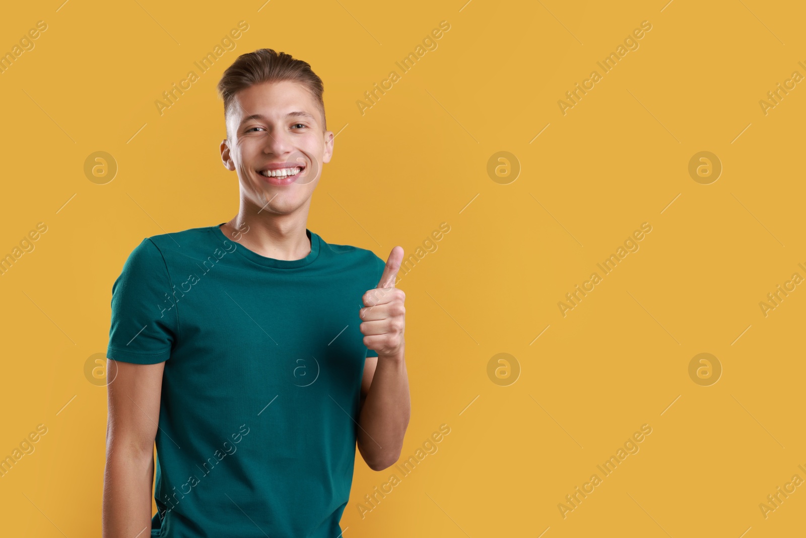 Photo of Happy man showing thumbs up on orange background, space for text. Like gesture