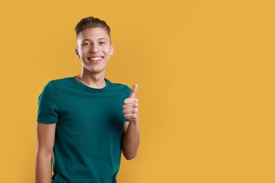 Photo of Happy man showing thumbs up on orange background, space for text. Like gesture