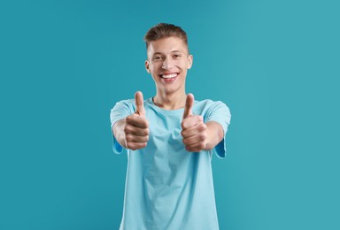 Photo of Happy man showing thumbs up on light blue background. Like gesture