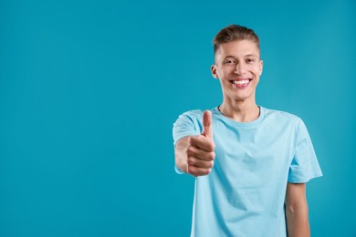 Photo of Happy man showing thumbs up on light blue background, space for text. Like gesture