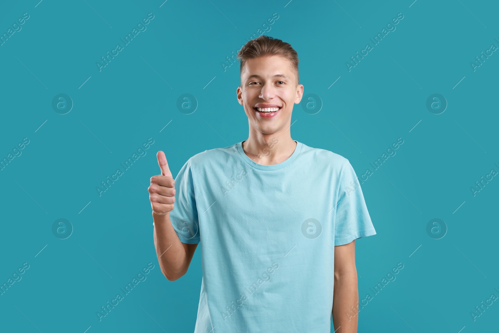 Photo of Happy man showing thumbs up on light blue background. Like gesture