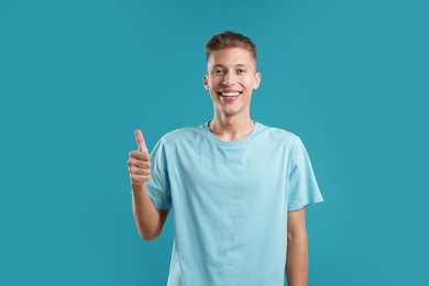 Photo of Happy man showing thumbs up on light blue background. Like gesture