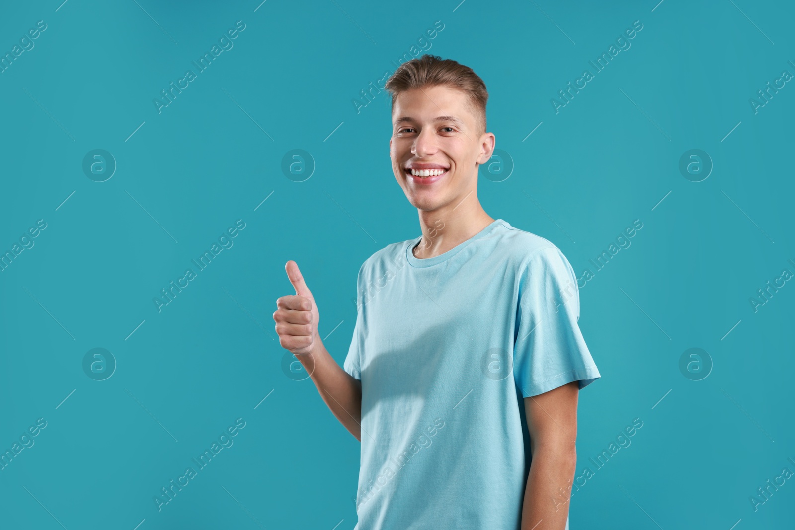 Photo of Happy man showing thumbs up on light blue background, space for text. Like gesture