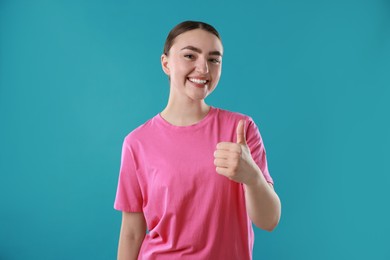 Photo of Happy woman showing thumbs up on light blue background. Like gesture