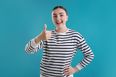 Photo of Happy woman showing thumbs up on light blue background. Like gesture