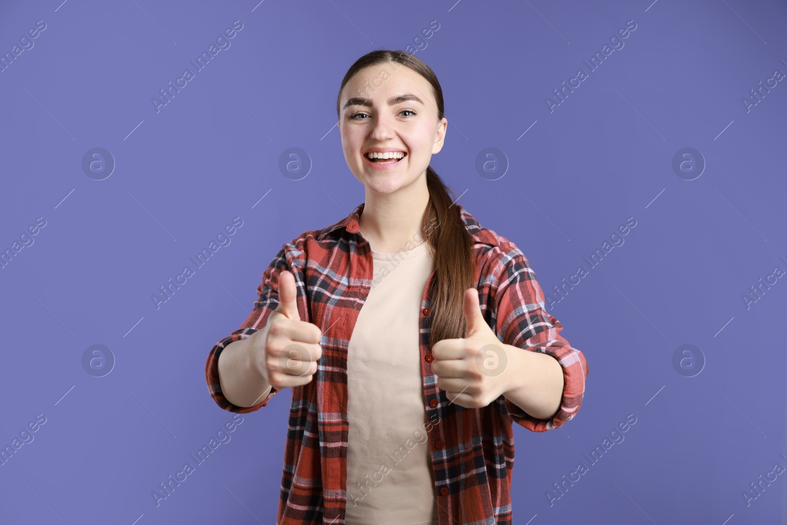 Photo of Happy woman showing thumbs up on purple background. Like gesture