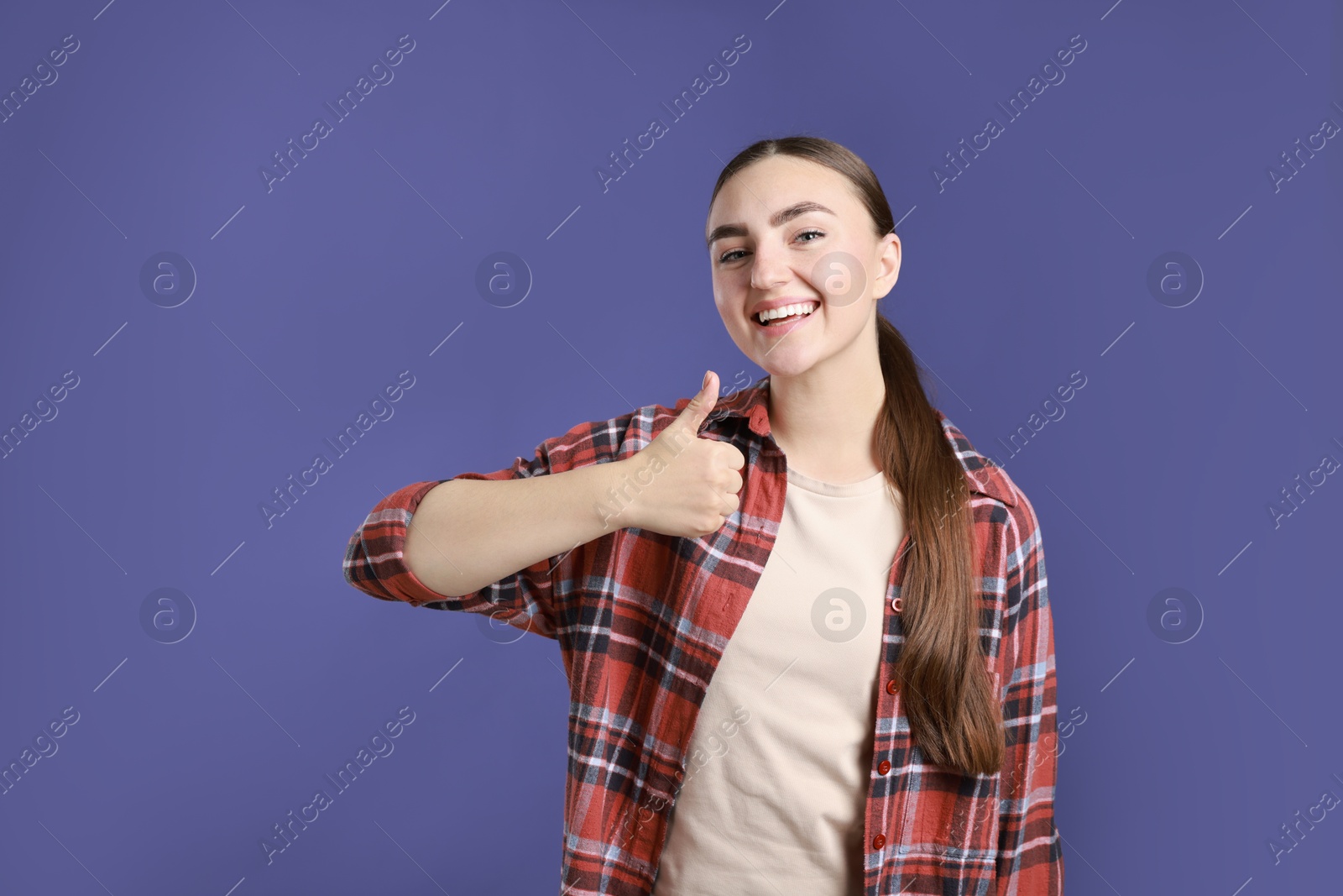 Photo of Happy woman showing thumbs up on purple background, space for text. Like gesture