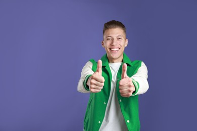 Photo of Happy man showing thumbs up on purple background, space for text. Like gesture