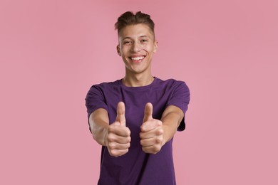 Photo of Happy man showing thumbs up on pink background. Like gesture