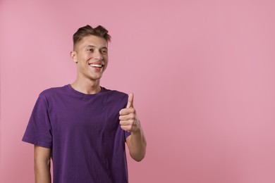 Photo of Happy man showing thumbs up on pink background, space for text. Like gesture